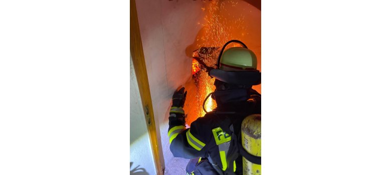 Auf dem Bild ist eine Einsatzkraft der freiwilligen Feuerwehr vor dem Kaminbrand zu sehen.