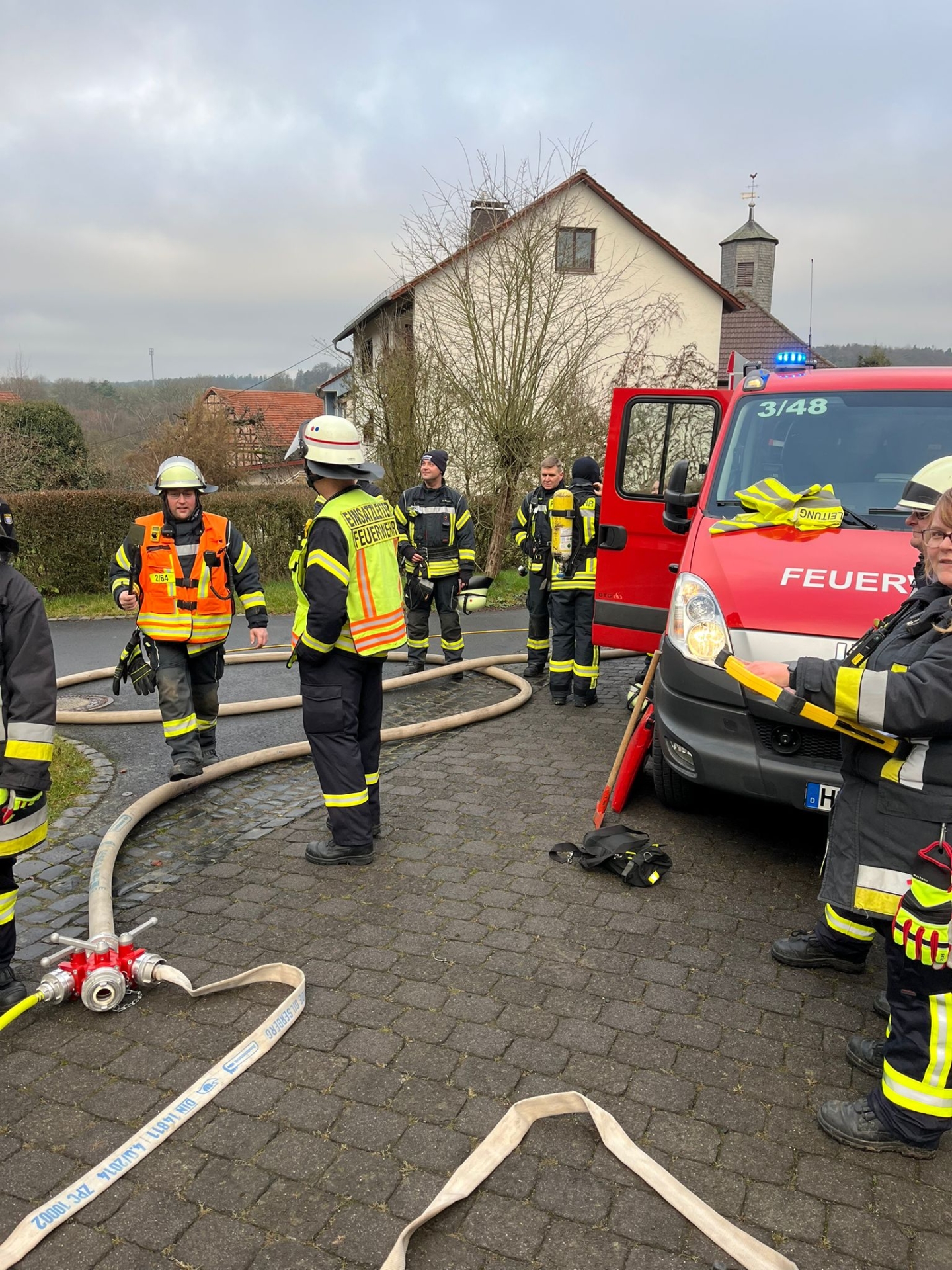 Auf dem Bild sind Einsatzkräfte der freiwilligen Feuerwehr bei einem Einsatz neben einem Einsatzfahrzeug zu sehen. 