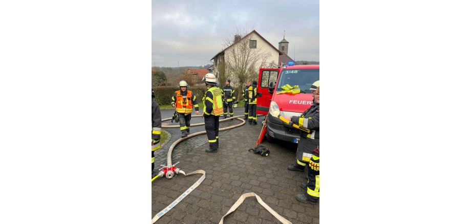 Auf dem Bild sind Einsatzkräfte der freiwilligen Feuerwehr bei einem Einsatz neben einem Einsatzfahrzeug zu sehen. 