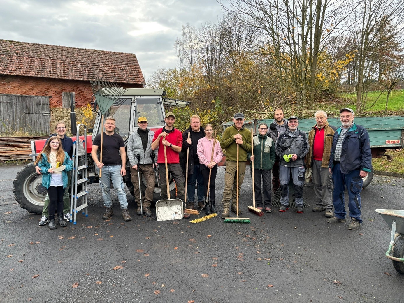 Es sind Personen vor einem Traktor zu sehen, die Besen in der Hand halten.
