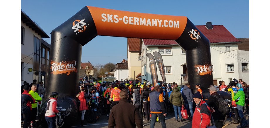 Es ist ein Bild des Startes bei einem der vergangen Bikemarathon zu sehen, auf dem Personen vor dem Start stehen. 