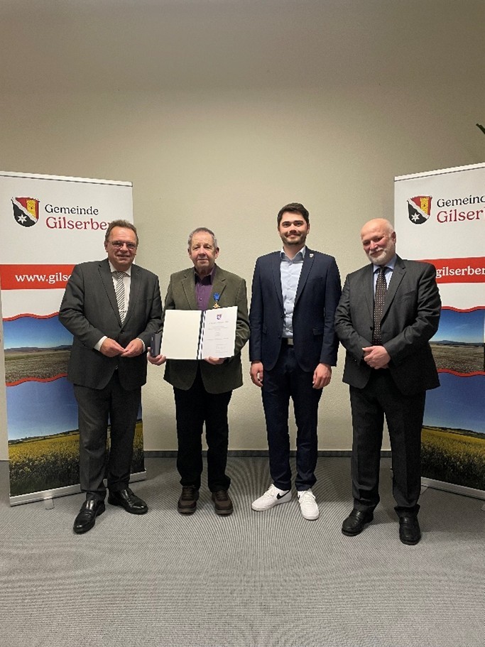 Von links nach rechts: Winfried Becker (Landrat), Klaus Böse (Geehrter), Lukas Daum (Bürgermeister) und Philipp Zmyi-Köbel (Leiter Amtsgericht Schwalmstadt); die Personen stehen vor einer weißen Wand.