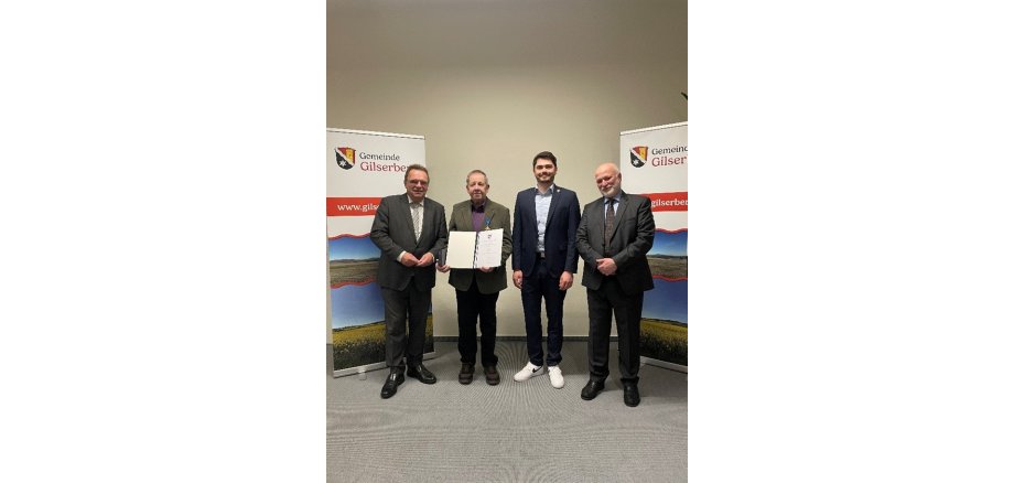 Von links nach rechts: Winfried Becker (Landrat), Klaus Böse (Geehrter), Lukas Daum (Bürgermeister) und Philipp Zmyi-Köbel (Leiter Amtsgericht Schwalmstadt); die Personen stehen vor einer weißen Wand.