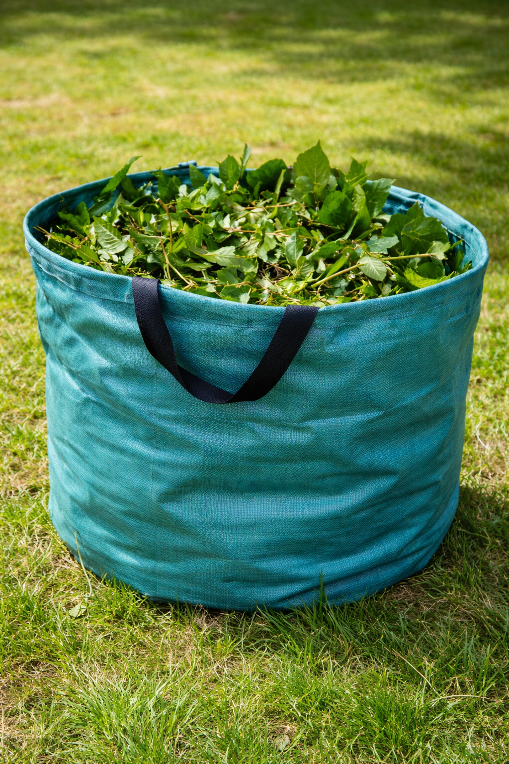 Es ist ein grüner Behälter mit Grünschnitt zu sehen; der Behälter steht auf einer Wiese.