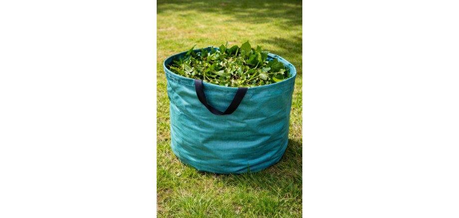 Es ist ein grüner Behälter mit Grünschnitt zu sehen; der Behälter steht auf einer Wiese.