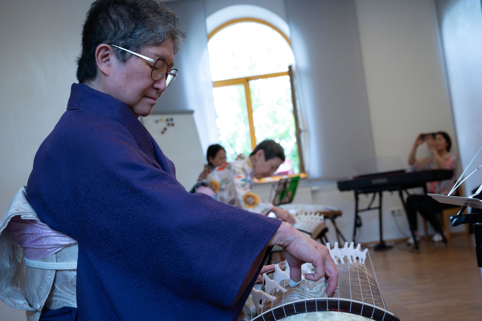 Im Vordergrund ist Frau Mizue Kishimoto-Angres am Koto, einem japanischen Instrument zu sehen.