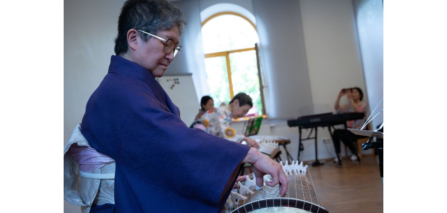Im Vordergrund ist Frau Mizue Kishimoto-Angres am Koto, einem japanischen Instrument zu sehen.