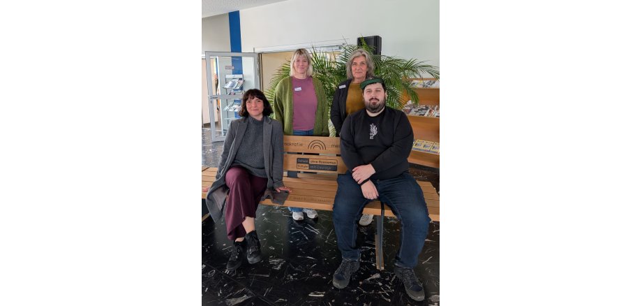 Netzwerkwerktreffen Schulen ohne Rassismus; Auf dem Bild sind vier Personen zu sehen, zwei sitzen auf einer Holzbank und zwei stehen hinter der Bank