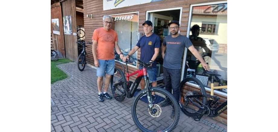 Auf dem Bild zu sehen: drei Männer mit einem Fahrrad vor dem Radgeschäft Freddys Zweiradshop