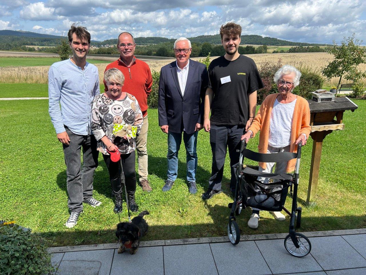 Auf dem Bild sind Personen auf einer Wiese zu sehen Zum Pressetermin im Hospiz trafen sich, v.l.n.r.: Lukas Stollenwerk (stellv. Hospiz-Einrichtungsleitung); Bettina Hainmüller mit Hündchen „Tammi“; Klaus Hainmüller; Lothar Vestweber (1. Vors. Förderverein Hospiz Kellerwald e.V.); Maximilian Feil (ehrenamtlicher Mitarbeiter Hospiz Kellerwald) und Heidemarie Rahmig (Hospizgast).