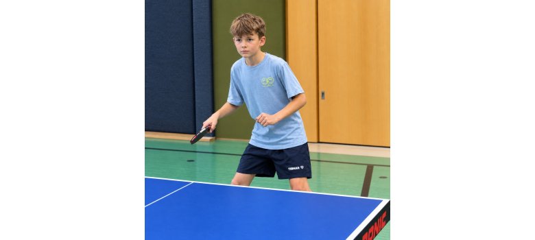 Johann Lecher spielt Tischtennis in einer Sporthalle und hält einen Tischtennisschläger in der Hand.